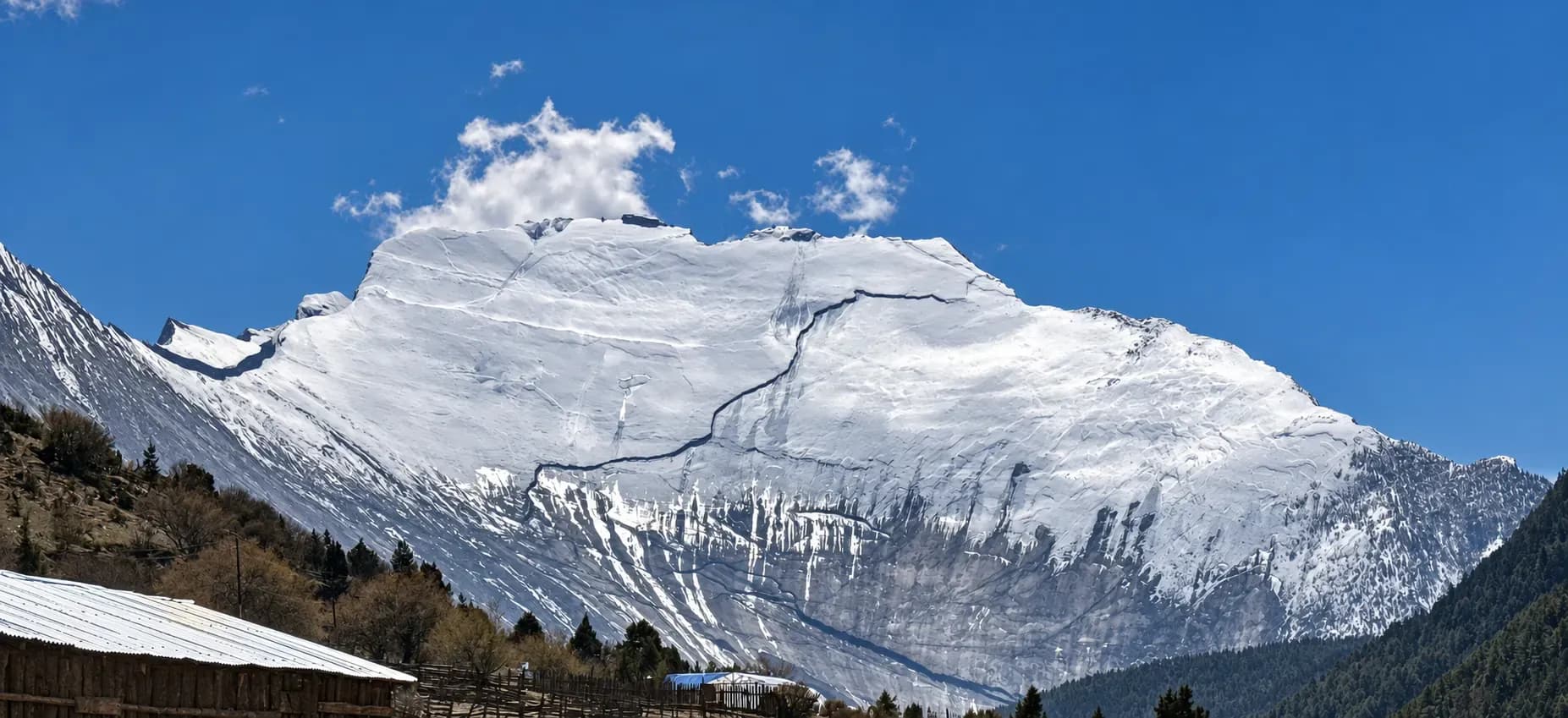 A broad snow-covered mountain above village rooftops in the Manang valley