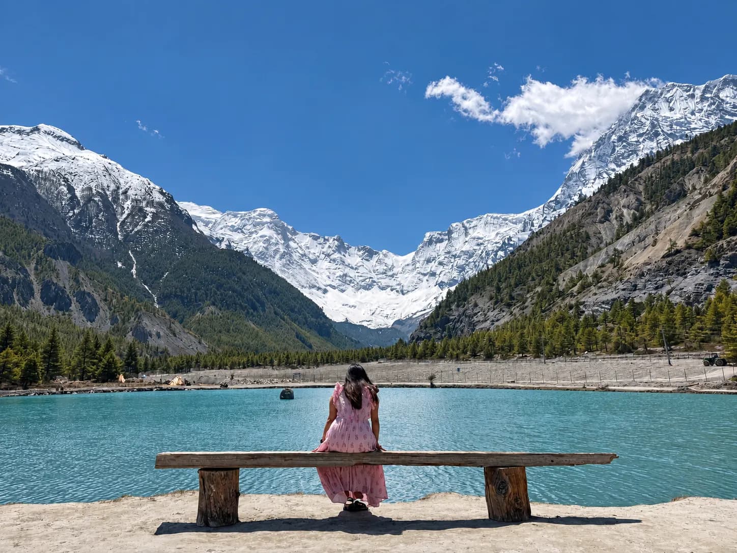 A traveller sitting beside a turquoise lake with snow-covered mountains beyond