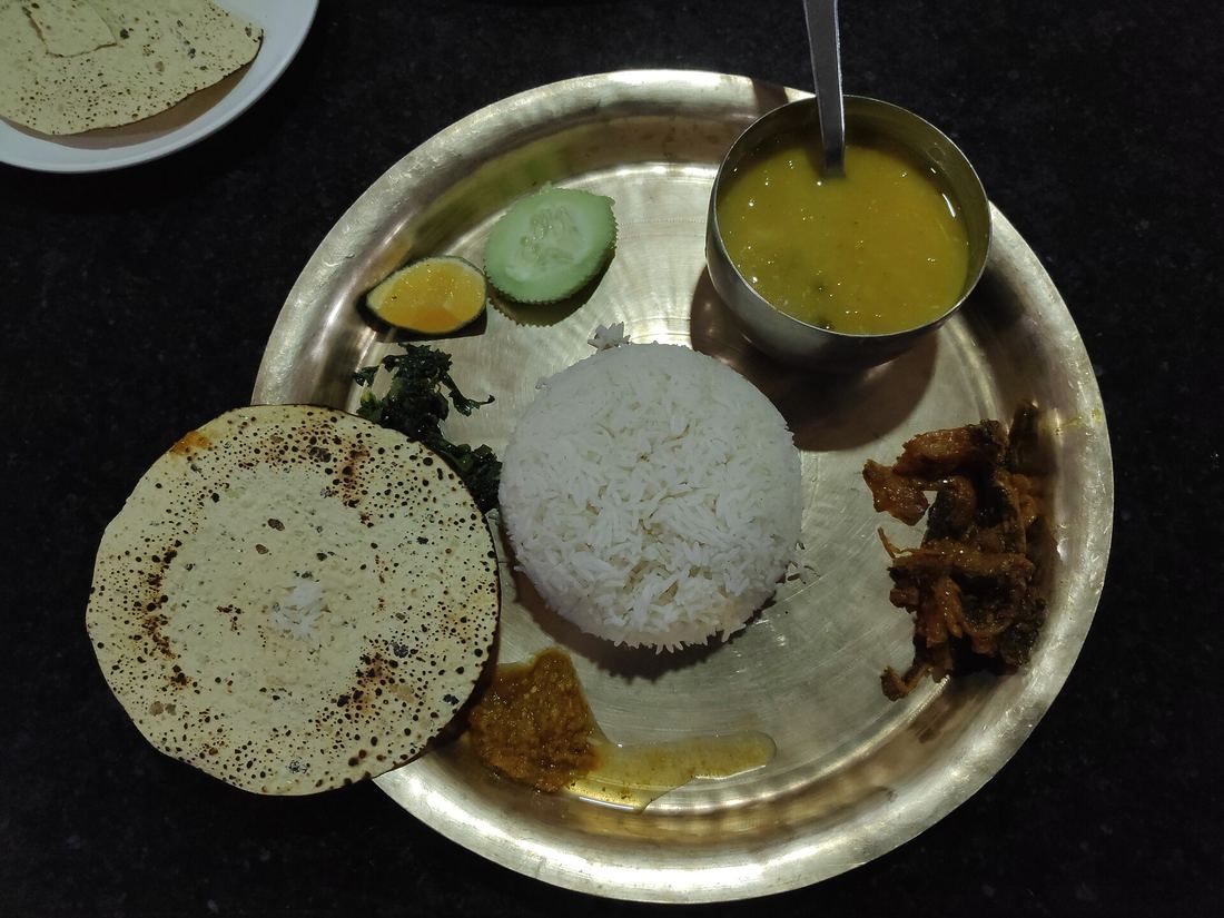 A steel plate of dal bhat tarkari, with rice in the centre surrounded by lentil soup, curried vegetables, greens and pickle in separate bowls