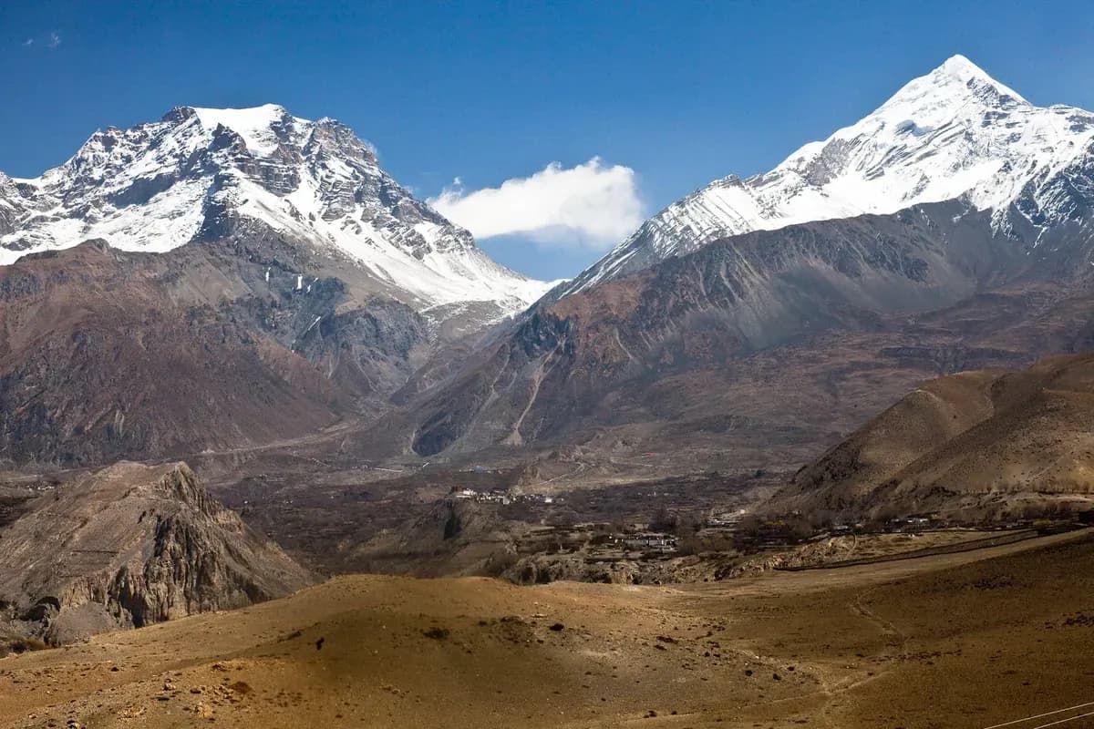 An arid valley and settlements lie below snow-covered mountains on the Muktinath side.