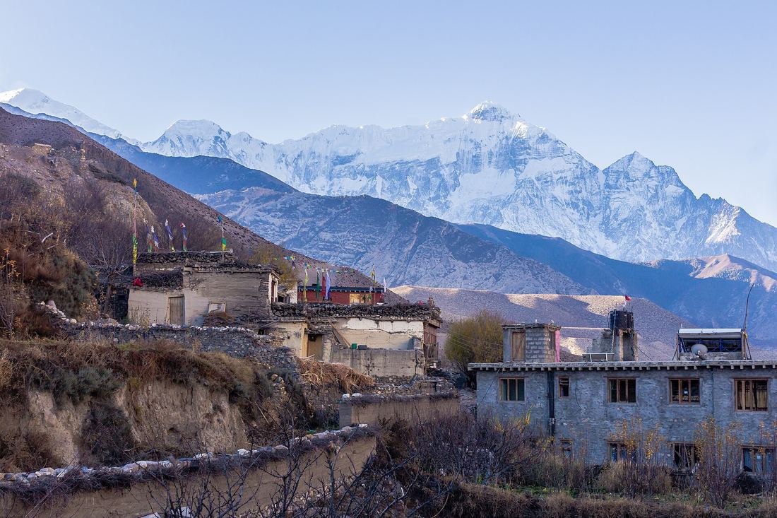 The village of Kagbeni in Mustang, its close-packed mud-brick houses and green barley fields set against bare, eroded desert cliffs under a wide sky